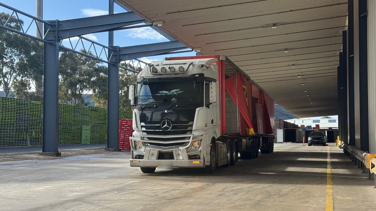 A prime mover with a red curtain-sided trailer under the awning of a loading dock