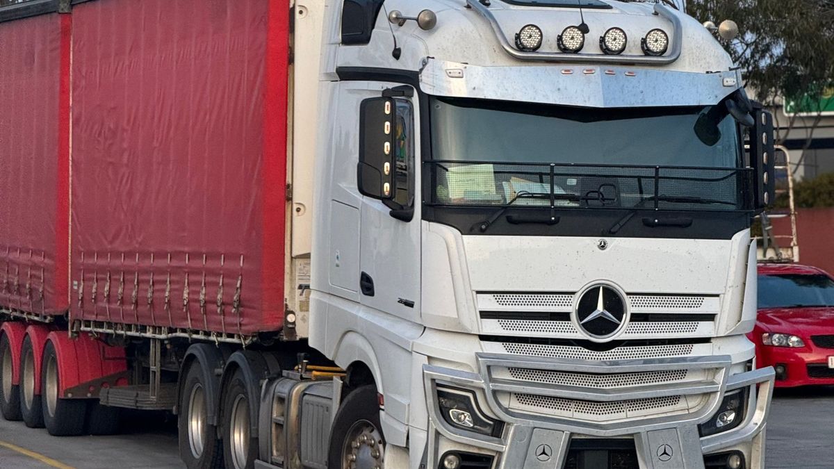 A Mercedes-Benz Actros prime mover with red curtain-sided trailers parked in a depot at dusk